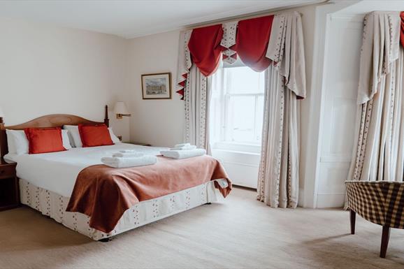 A cozy hotel room with a comfortable bed, a chair, and a window offering a scenic view.