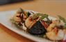 A white plate with neatly arranged Hebridean scallops, Stornoway black pudding, and mixed greens on a wooden surface.