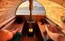 2 people sitting inside a barrel sauna looking out to the sea