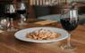 Plate of pasta and a glass of wine set on a table.