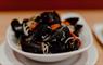 A white bowl filled with Hebridean mussels, garnished with diced tomatoes, parsley, and linguine.